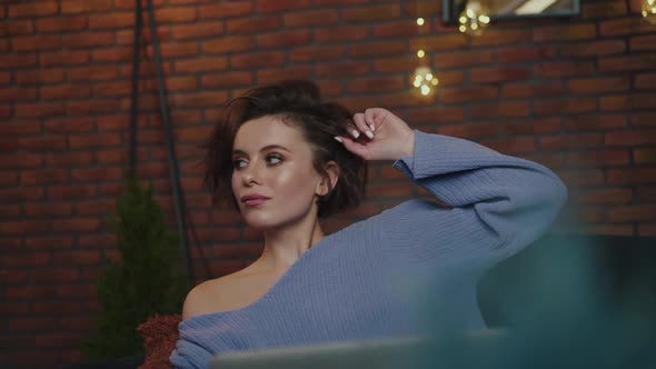 Glamorous Girl Relaxing on Cozy Sofa and Uses Laptop in Evening alt