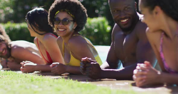 Diverse group of friends standing at the poolside talking and looking at the camera alt