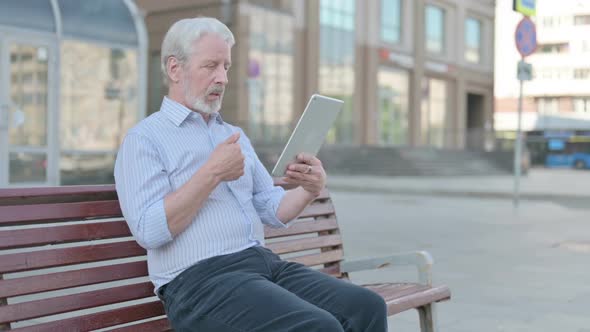 Online Video Chat on Tablet By Old Man Sitting Outdoor on Bench alt