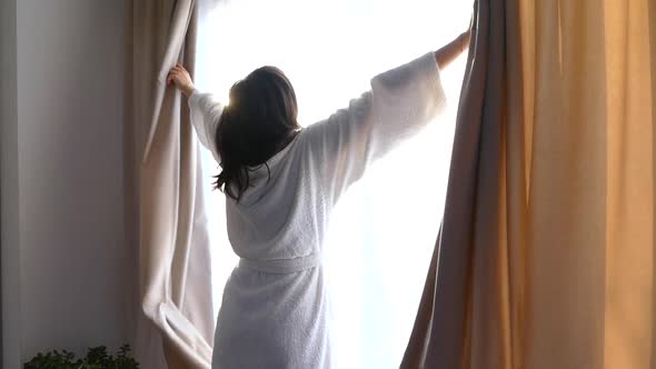 A Girl in a White Coat Opens the Curtains. In the Morning Stretch By the Window