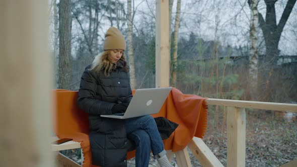 Woman in a Down Jacket Winter Hat and Gloves Works on a Laptop