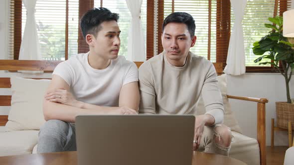 asian gay couple sit couch use laptop facetime video call with friends and family in living room.
