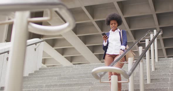 African american businesswoman walking and holding smartphone alt