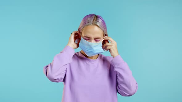 Young Pretty Teenager Girl Puts on Face Medical Mask During Coronavirus Pandemic. Portrait on Blue alt