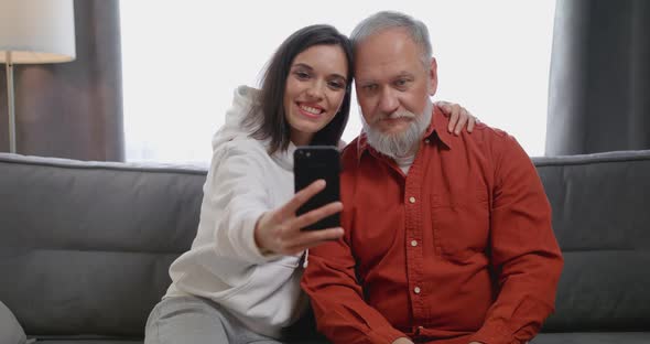Happy Older 80s Grandfather Posing for Selfie Shot on Cellphone with Smiling Attractive Grownup alt