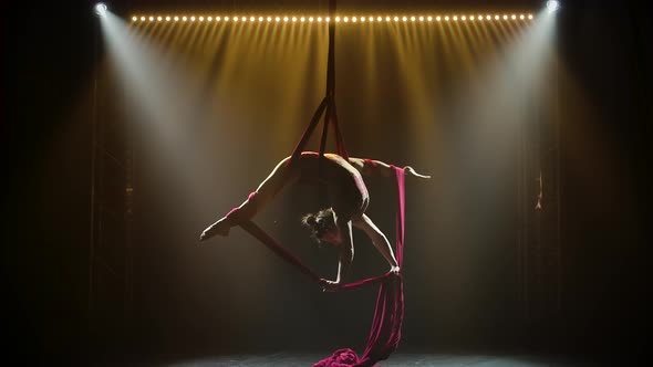 Equilibrium Gymnast Stretched and Rotating on a Red Silk. Silhouette Young Girl Performs the alt