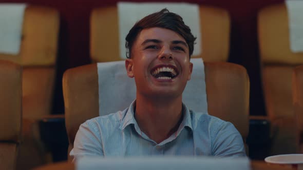 Attractive cheerful young caucasian man laughing while watching film in movie theater.