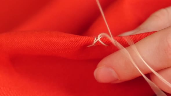 Woman`s Hands Sewing with Needle, White Thread and Thimble on Red Cloth, Close Up, Slow Motion alt
