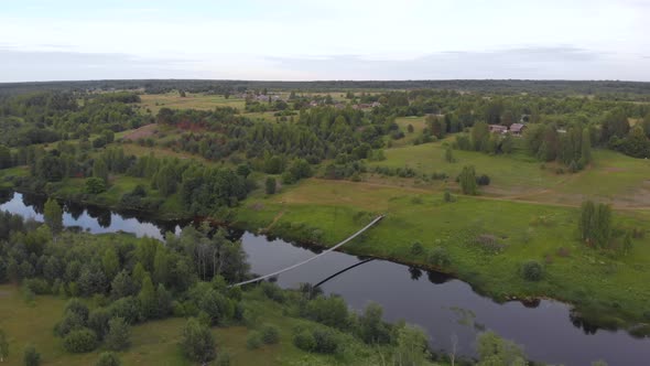 Suspended Bridge Approach on Remote Russian River with Distant Village Aerial alt