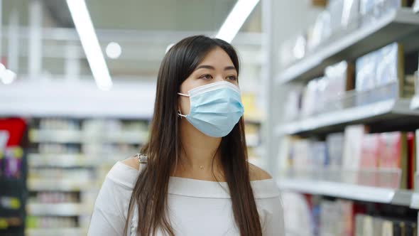Asian Woman in Mask Looking at Shelves at Store alt