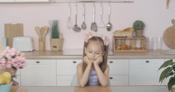 Sad Little Caucasian Girl Sitting at the Table with Head on Hands As Twin Brothers Coming with Gift alt