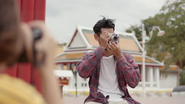 Tourists Asian man using film camera taking a photo while sitting on the street in Thailand.