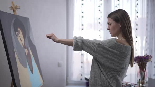 Focused Confident Woman Painting Picture Stretching Hand Looking at Brush Standing at Easel alt