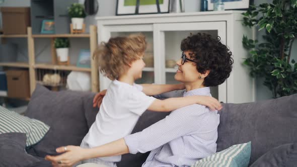 Slow Motion of Loving Mother and Little Son Hugging Sitting on Sofa at Home alt