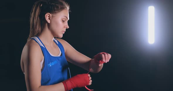 Medium Shot A Beautiful Female Boxer Pulls Red Bandages Onto the Wrist of a Female Fighter alt