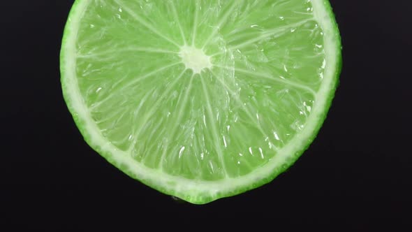 Water drop falling from green hue lime on black background. Lime slice and water splashing, drops alt