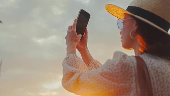 A young tourist in a hat taking a photo of the Motherland on a smartphone on the Mamayev Kurgan alt