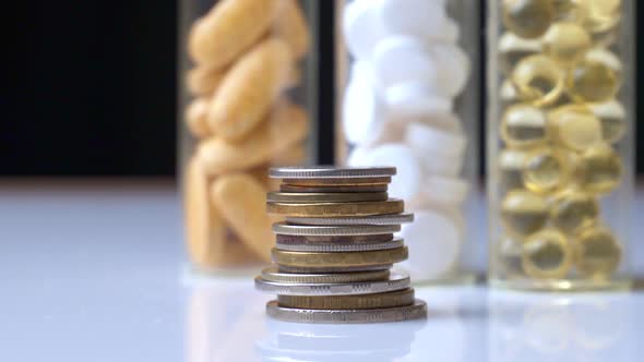 A Stack of Coins Against the Background of Three Jars of Pills alt