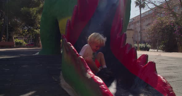 Happy child comes down the high dragon children's slide and runs on summer day alt