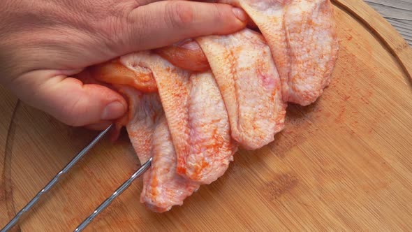 Male Hands Are Piercing the Raw Chicken Wings with Skewers on the Wooden Board alt