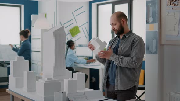 Man Engineer Designing Blueprints Plans of Construction with Building Model in Office alt