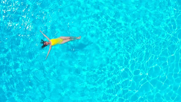View From the Top As a Woman in a Yellow Swimsuit Lying on Her Back in the Pool alt