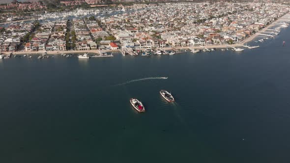 Aerial shot orbiting around two ferries crossing paths in Newport Harbor with anchored boats and bui alt
