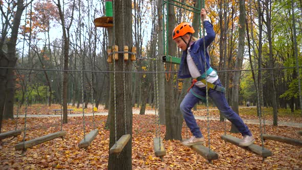 Little girl in orange helmet and protective gear on rope-way in autumn  forest.