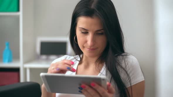 Brunette Women Using a Tablet Pc Sitting on the Sofa in a Living Room alt