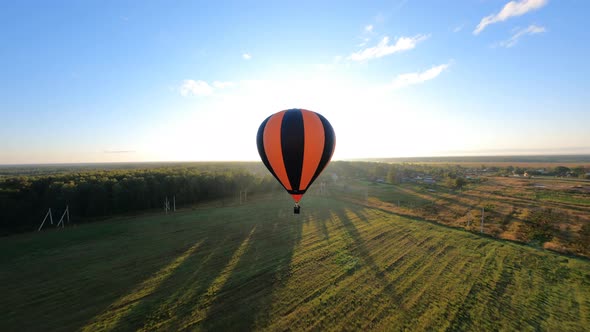 Orange Hot air ballon floating above sloping field at beautiful sunrise