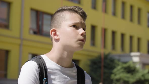 A Caucasian Teenage Boy Looks Around  Closeup  a School in the Background