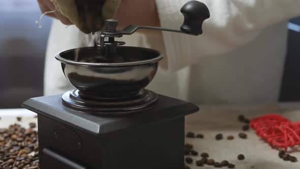A Man in a White Coat in the Morning Pours Coffee Beans Into a Retro Coffee Grinder From a Fabric