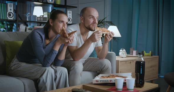 Happy couple sitting on the couch and eating pizza