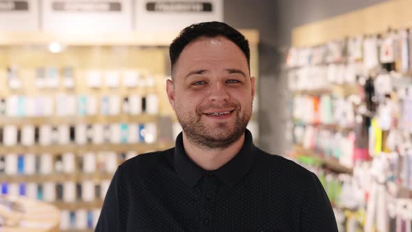 Smiling Caucasian Millennial Seller Man in Electronics Store Looking at Camera