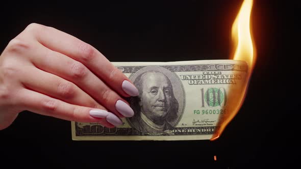 Woman Holding Burning American Hundred Dollar Banknote on Black Background alt