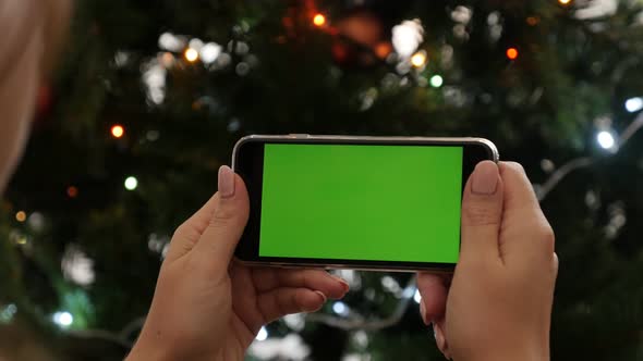 Woman holds modern smart phone  on New Year night 4K 2160p 30fps UltraHD footage - Christmas tree li