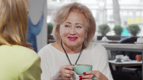 Lovely Senior Woman Laughing Talking To Her Daughter Over Cup of Tea alt