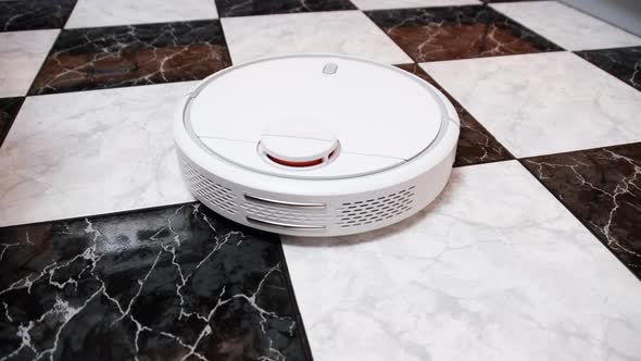 The Robot Vacuum Cleaner Cleans in the Modern House on the Tiles Floor at Kitchen alt