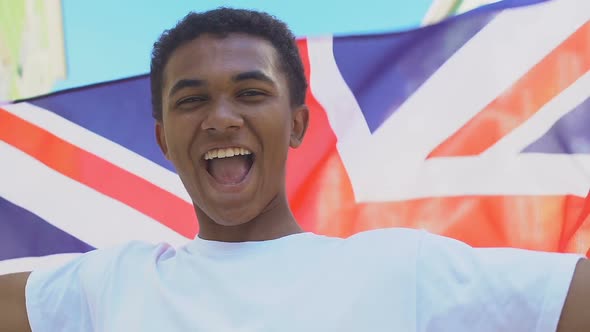 Extremely happy Afro-American male teenager waving British flag alt