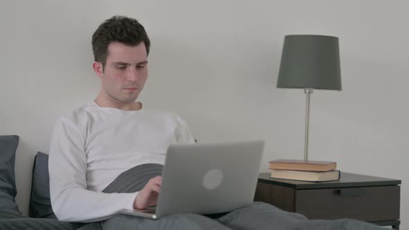 Man with Back Pain Working on Laptop in Bed alt