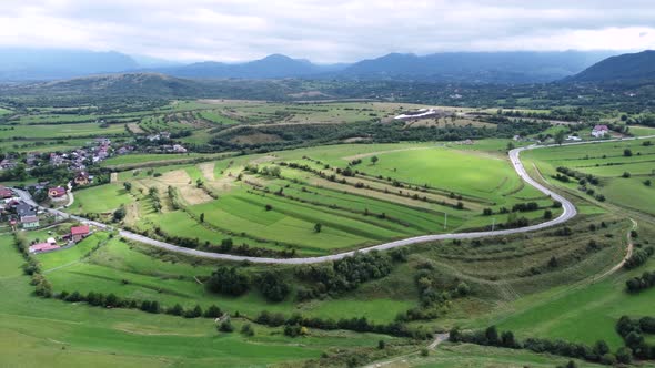 Aerial Wide Open View of Mountain Empty Road Close to a Romania Village alt