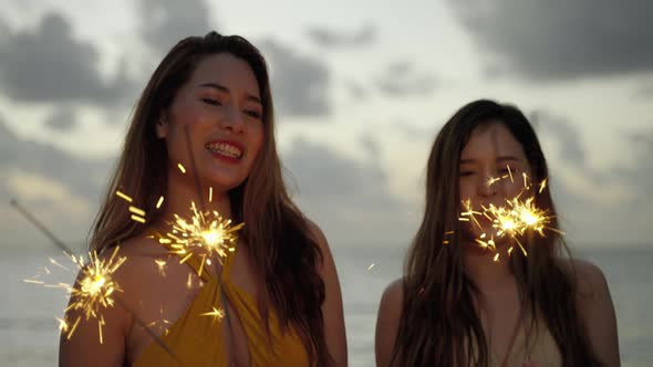 beautiful asian woman and her friends are having fun playing sparklers on the beach during Twilight