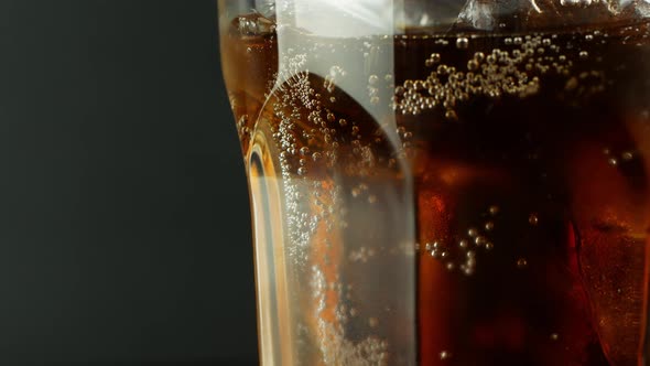 Pouring cola with ice cubes close-up. Cola with Ice and bubbles in glass on a black background. alt