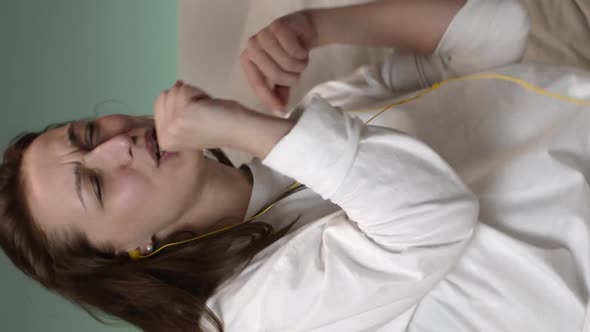 Vertical Shot Happy Woman with Yellow Headphones Listening Music on Bed at Home and Smiling