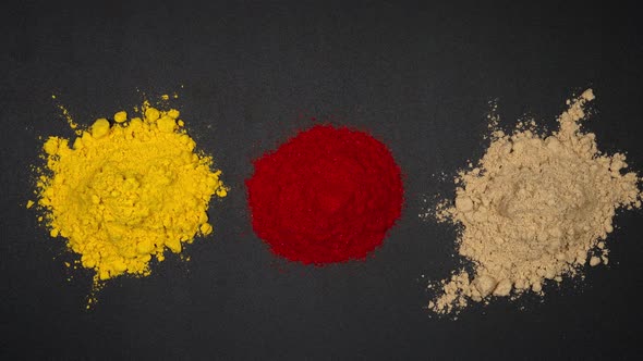 Three pile of powder of red pepper, ginger and turmeric on a black table