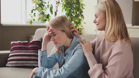 Upset Carrying Mature Mother Cuddling Hugging Soothing Crying Grown Up Daughter Sitting on Couch at alt