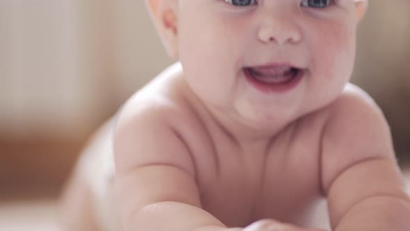 A little baby is lying on his belly against a light background and smiling alt