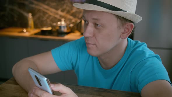 Attractive Man in a White Hat Sits at the Table Uses a Mobile Phone