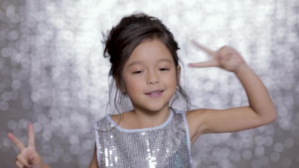 Beautiful Smiling Little Child Girl in a Silver Dress Dancing on Background of Silver Bokeh.