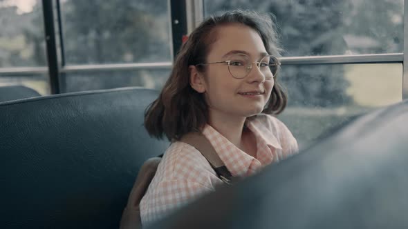 Smiling School Girl Sitting at Bus Window in Glasses alt